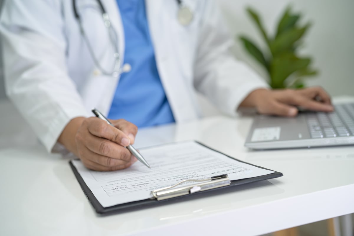 Doctor Write Health Medical Note in Clipboard with Laptop in Hos